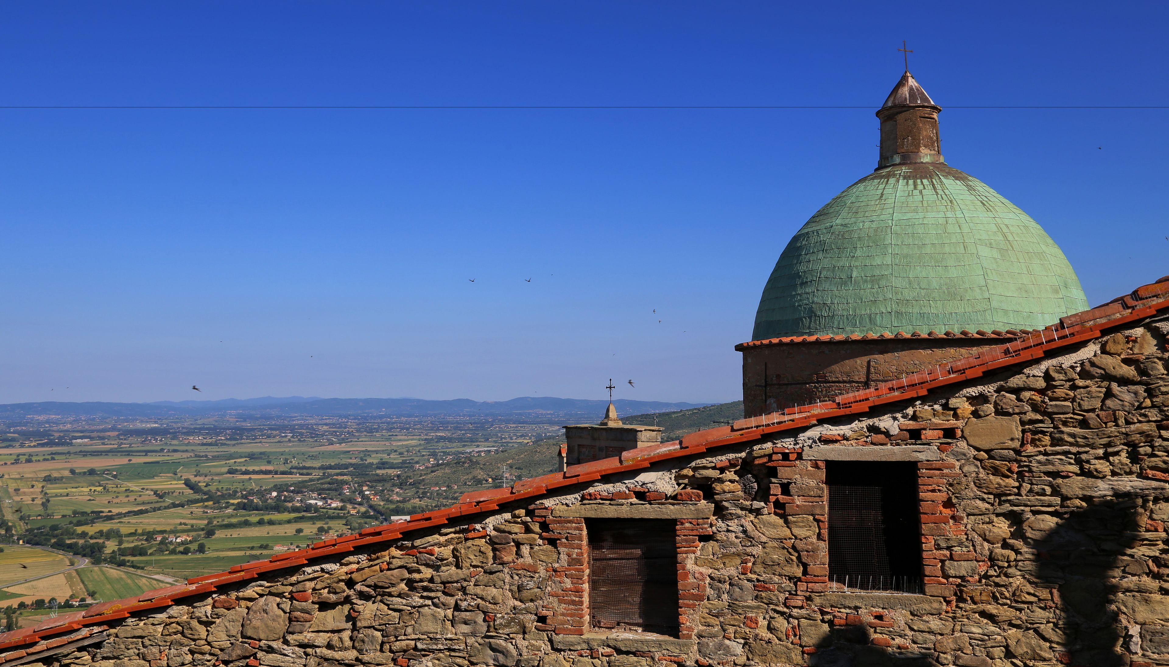 Un edificio de piedra con una cúpula verde y una cruz en la parte superior, con vistas a un valle.