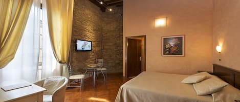 Un dormitorio con cama, escritorio, silla, televisor y pared de piedra.