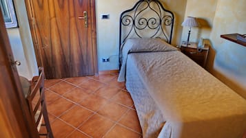Een slaapkamer met een houten deur, een metalen bedframe, een nachtkastje met een lamp en een betegelde vloer.
