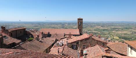 A view of terracotta-tiled rooftops with a prominent tower structure, overlooking a rural landscape.