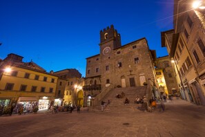 Uma praça histórica com uma torre do relógio imponente, ruas de calçada e edifícios tradicionais.