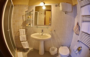 Egy fürdőszoba, amelyben van egy lábas mosdókagyló, egy WC, egy tükör és egy törölközőtartó, amelyen több törölköző is található.