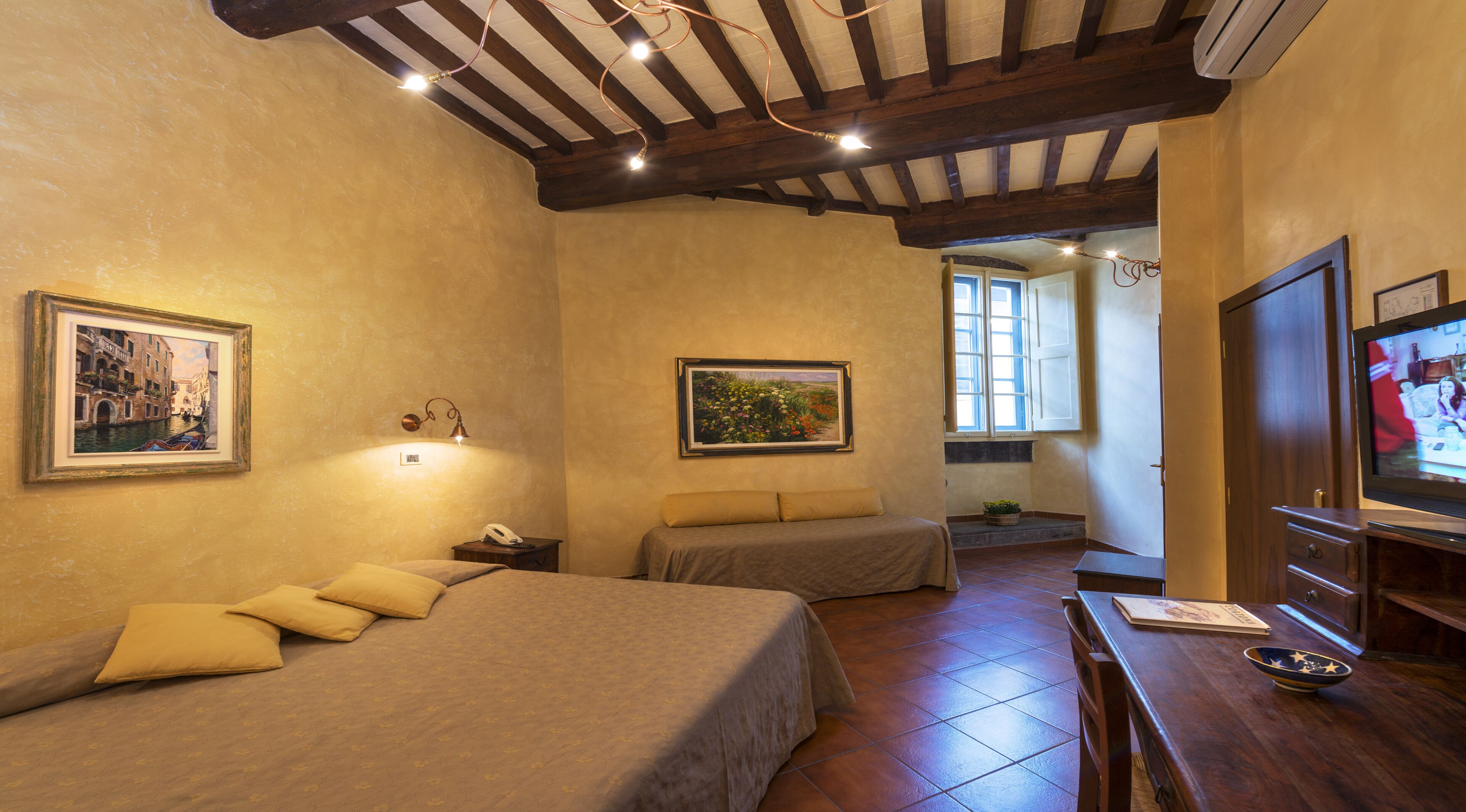 Une chambre à coucher avec un lit, des tables de chevet, un téléviseur et deux tableaux accrochés au mur.