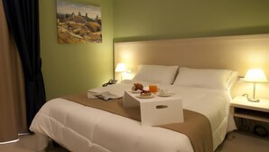 A hotel room with a bed, bedside lamps, a small table with a newspaper, a glass of orange juice, and a painting on the wall. - Tiziano Hotel (Trapani)