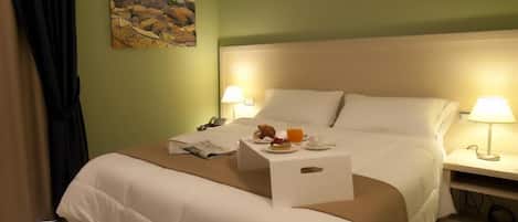 A hotel room with a bed, bedside lamps, a small table with a newspaper, a glass of orange juice, and a painting on the wall.