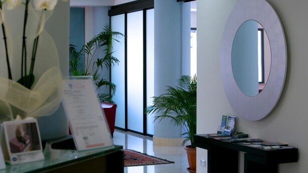 A reception area with a glass counter, a large mirror, and potted plants. - Tiziano Hotel (Trapani)