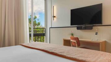 Ein Hotelzimmer mit Bett, Schreibtisch mit Stuhl, Fernseher und einem Fenster mit Vorhängen.