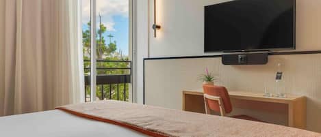 A hotel room with a bed, a desk with a chair, a television, and a window with curtains.
