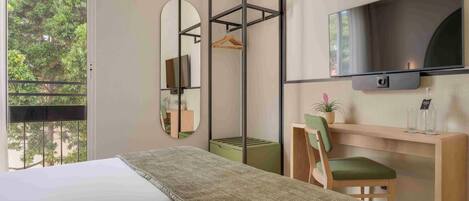 Een moderne hotelkamer met een groot bed, een bureau met stoel, een aan de muur bevestigde televisie en een groot raam met uitzicht op bomen.