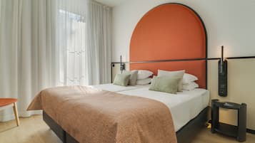 Una habitación de hotel moderna con una cama grande, un cabecero curvo y una mesita de noche con una lámpara.