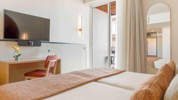 Habitación de hotel con cama, escritorio y silla, televisor y puerta corrediza a un balcón.
