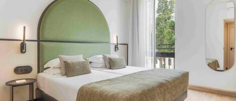 Un dormitorio moderno con una cama grande, cabecera verde, una mesita de noche y un ventanal con vistas a árboles.