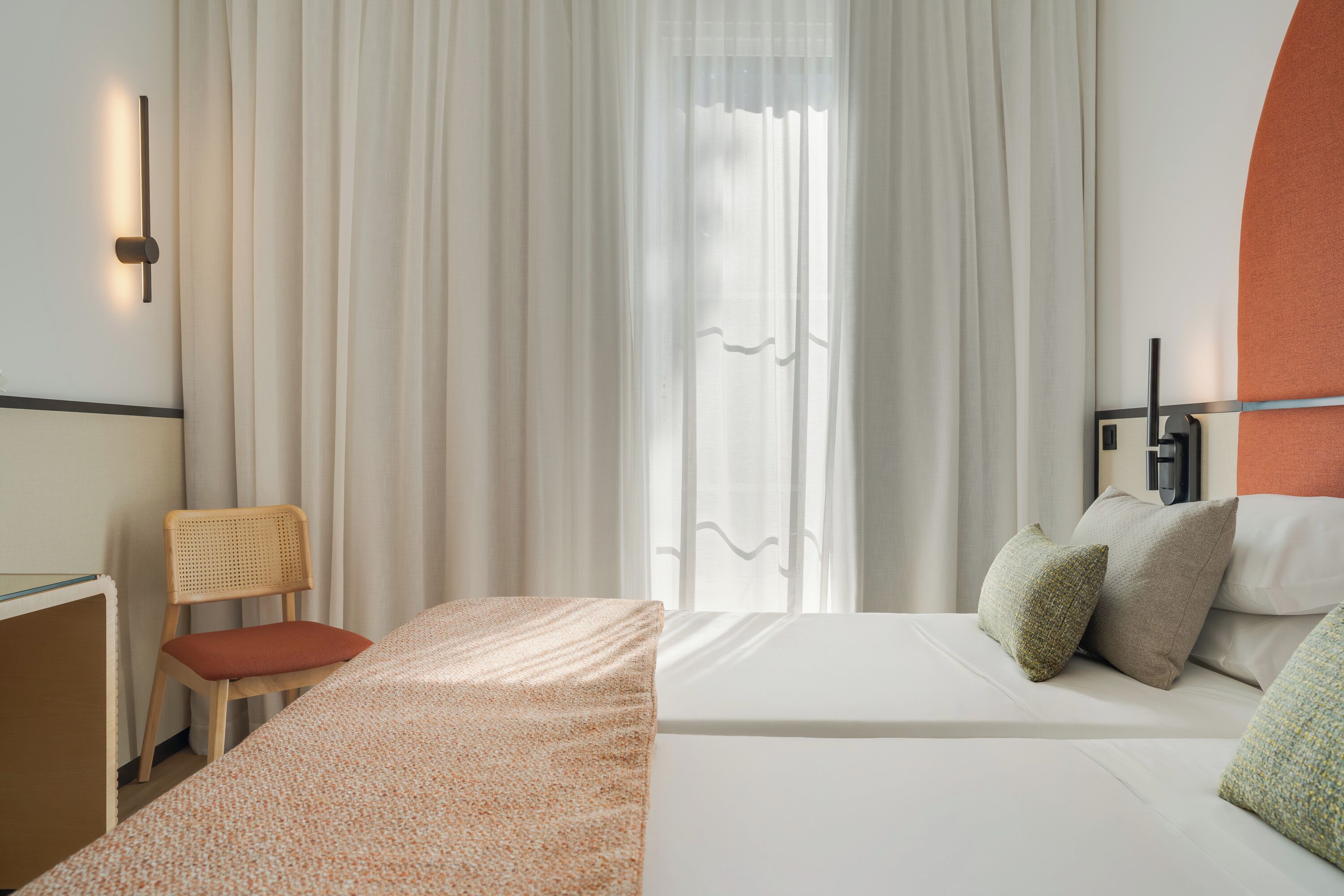 Quarto de hotel com cama, uma cadeira e uma escrivaninha.