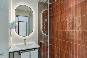Un baño con un lavamanos blanco, un espejo redondo y una ducha con puerta de vidrio.