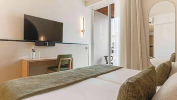 A hotel room with a bed, a desk, a chair, a TV, and a sliding door to a balcony.
