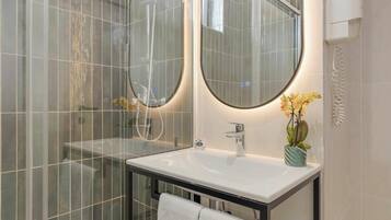 A modern bathroom with a glass shower enclosure, a white sink with a single faucet, and a round mirror above it.