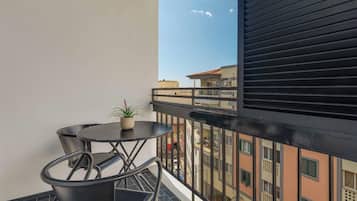 Un balcón con una mesa redonda y sillas, una planta en maceta y vistas de edificios vecinos.
