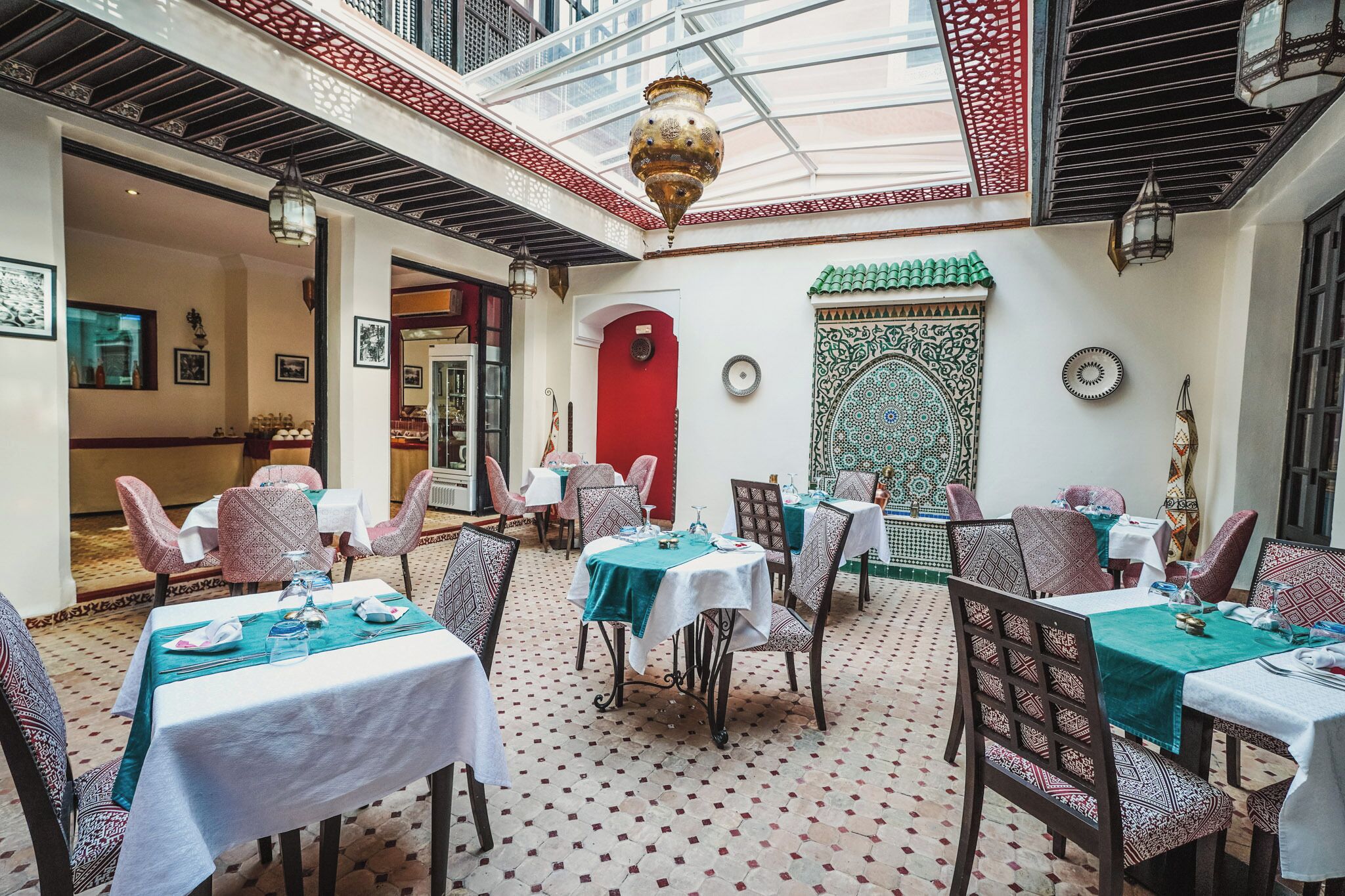 An indoor dining area with tables set for guests, featuring patterned chairs and a tiled floor.