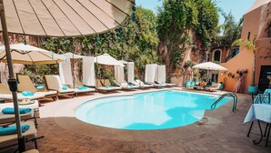 A poolside area with lounge chairs and umbrellas, surrounded by brick flooring and greenery.