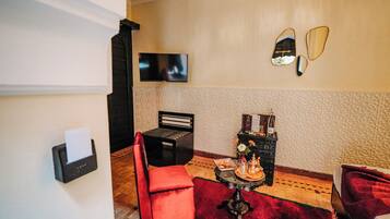 Ein Zimmer mit Flachbildfernseher, einem roten Sessel, einem kleinen Tisch mit Tablett und einem dekorativen Spiegel an der Wand.