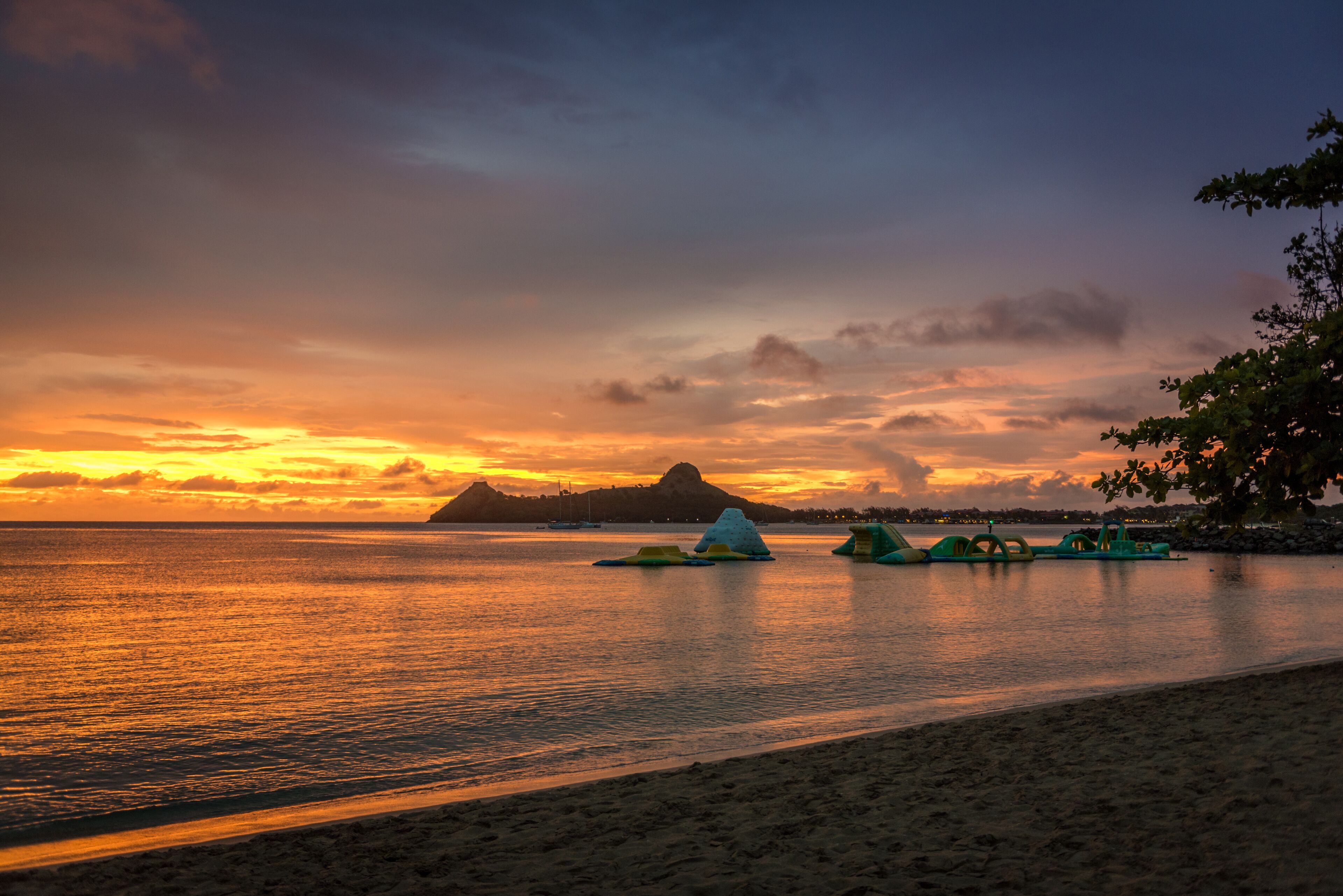 Uma praia com um pôr do sol, águas calmas e uma montanha ao longe.