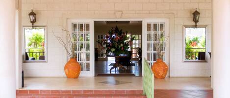 A hotel entrance with a tiled floor, a central doorway, and two large potted plants on either side.