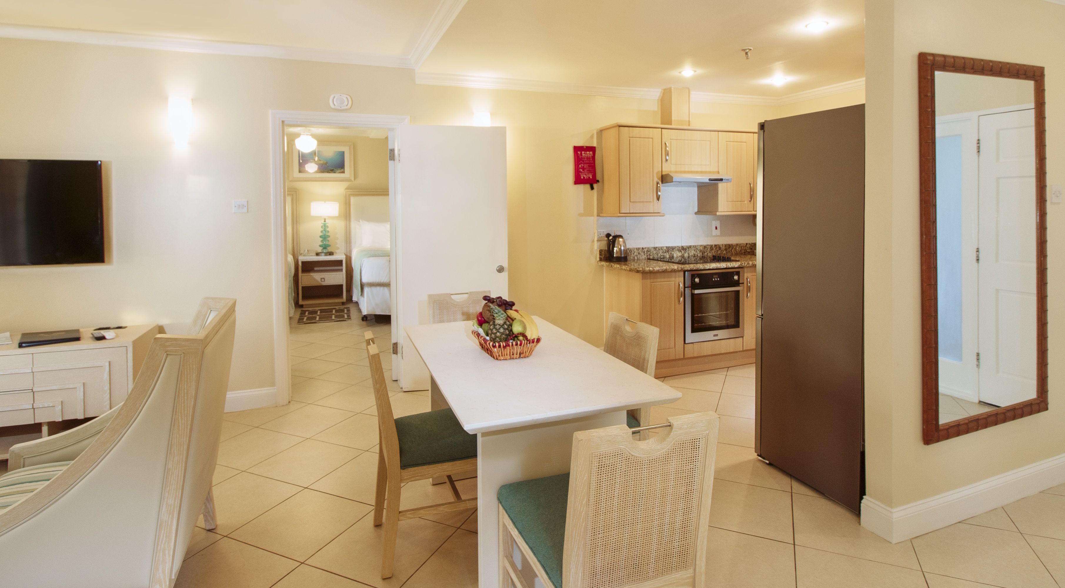 A compact kitchen with a dining area, a TV mounted on the wall, and a small refrigerator.