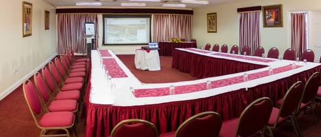 A conference room with a long table, red chairs, a projector screen, and a whiteboard.
