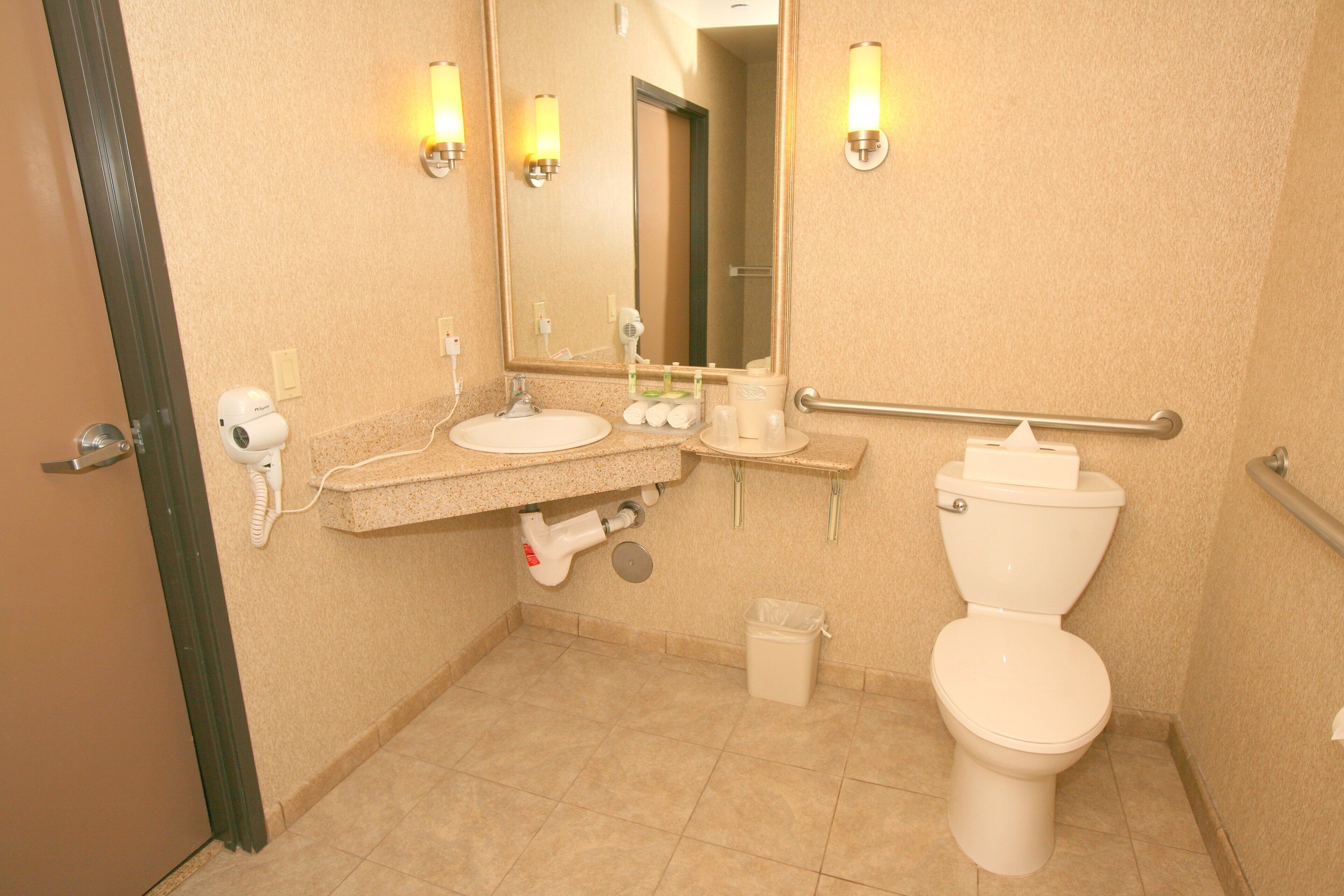 A bathroom with a sink, mirror, toilet, and hand dryer.