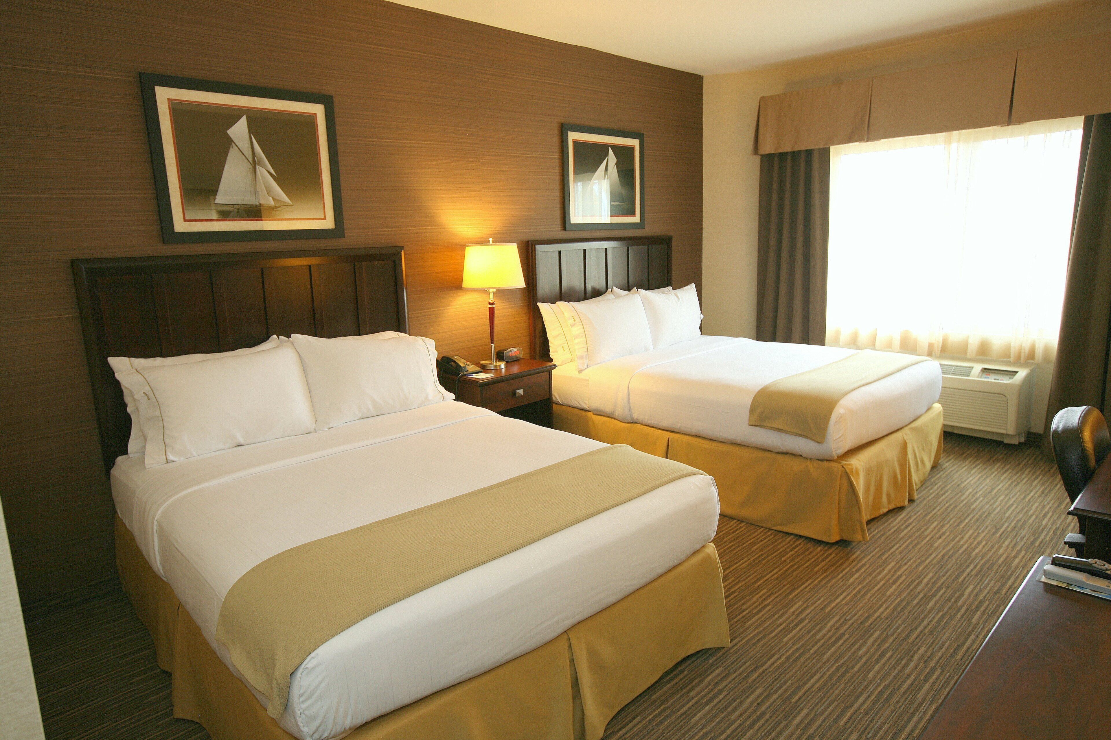 A hotel room with two beds, a nightstand, a lamp, a framed picture, and a window with curtains.