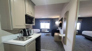 Une chambre d’hôtel compacte comprenant un coin cuisine, un lit, un petit espace salon et une fenêtre laissant entrer la lumière naturelle.
