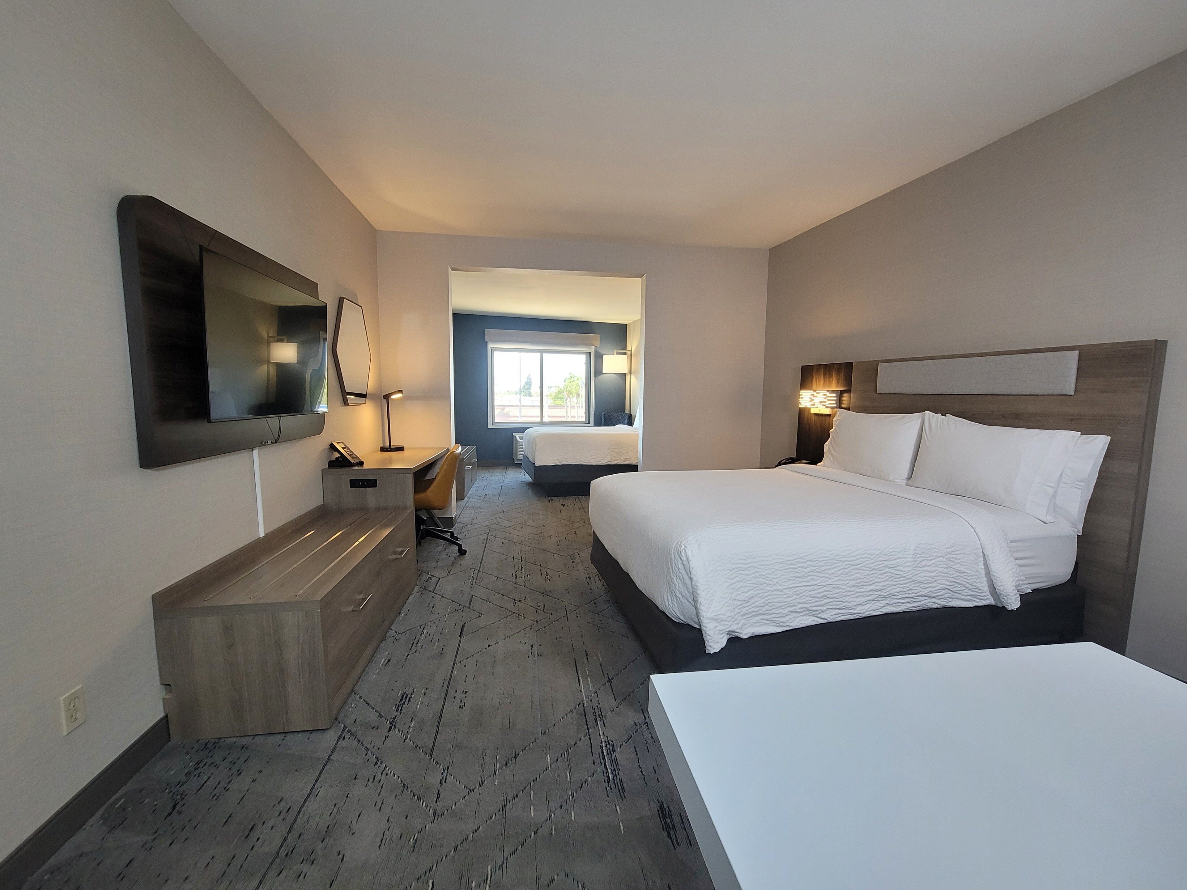 Een hotelkamer met een groot bed, een bureau met stoel, een aan de muur bevestigde televisie en een raam met uitzicht.