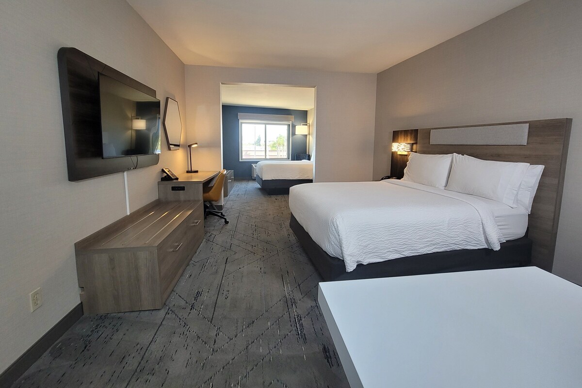 Habitación de hotel con una cama grande, un escritorio con silla, televisor montado en la pared y ventana con vistas al exterior.