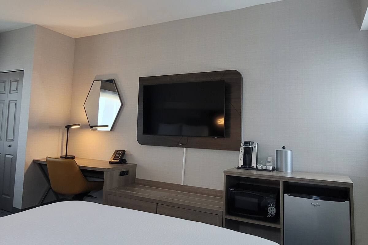 A hotel room with a bed, a desk with a telephone, a coffee maker, a microwave, and a TV mounted on the wall.