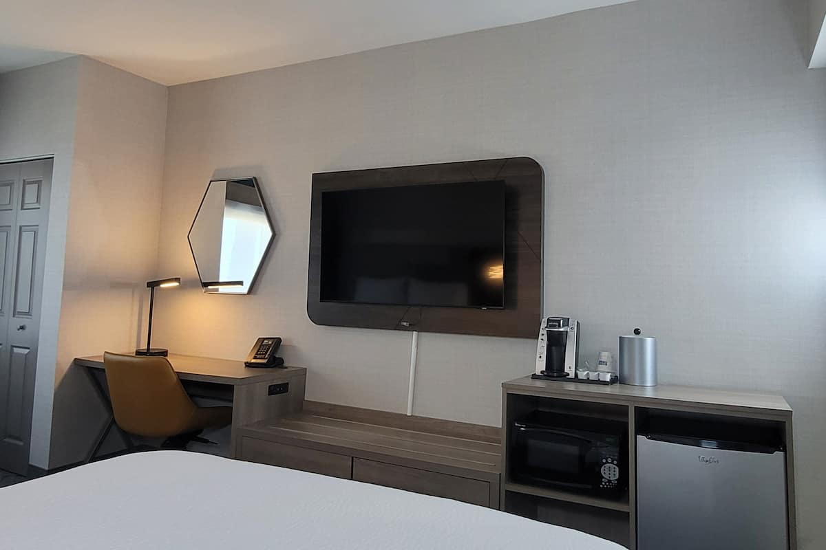 Une chambre d’hôtel équipée d’un lit, d’un bureau avec un téléphone, d’une machine à café, d’un four à micro-ondes et d’un téléviseur fixé au mur.