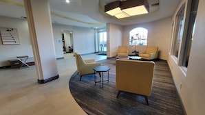 Un hall d’entrée avec une moquette aux motifs courbes, deux fauteuils, une petite table et une grande fenêtre laissant entrer la lumière naturelle.