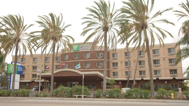 Un bâtiment de l’hôtel Holiday Inn Express, avec une entrée bien visible, des palmiers et un ciel dégagé.