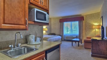 Habitación de hotel con kitchenette, cama, televisor y ventana con cortinas.