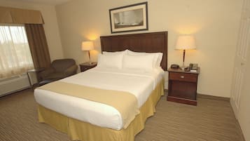 Quarto de hotel com cama grande, duas mesas de cabeceira com abajures, uma poltrona, janela com cortinas e um quadro na parede.