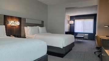Habitación de hotel con dos camas, un escritorio, una silla y una ventana con persianas.