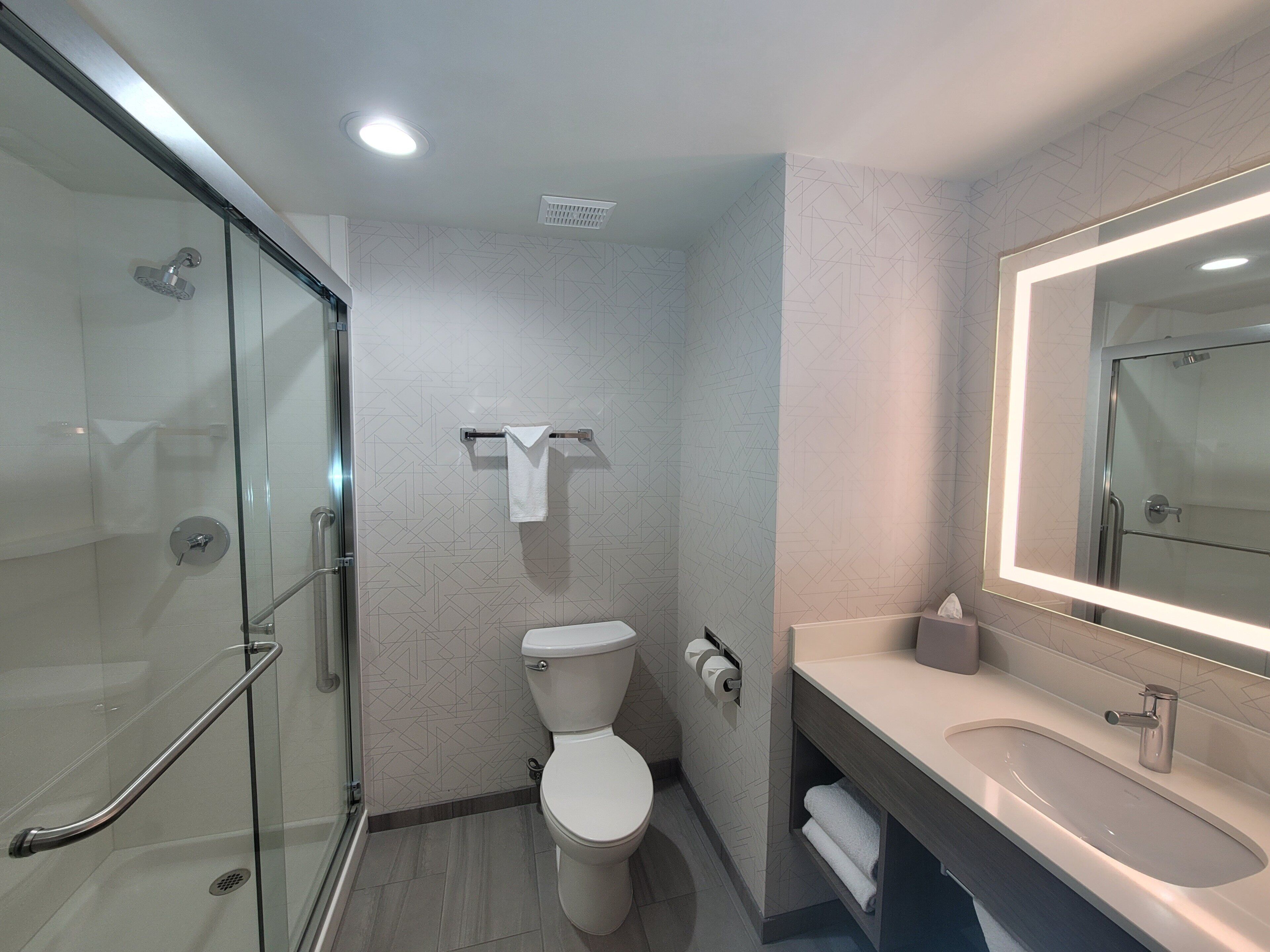 Un baño moderno con cabina de ducha de vidrio, inodoro y tocador con espejo.