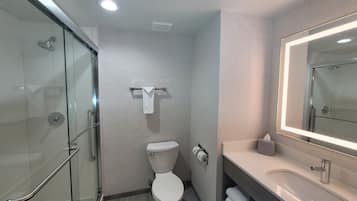 Un baño moderno con cabina de ducha de vidrio, inodoro y tocador con espejo.