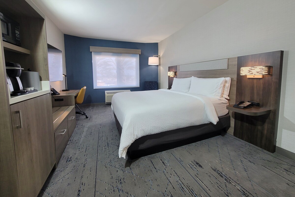 Una habitación de hotel moderna con una cama grande, un escritorio, una silla y una ventana con persianas.