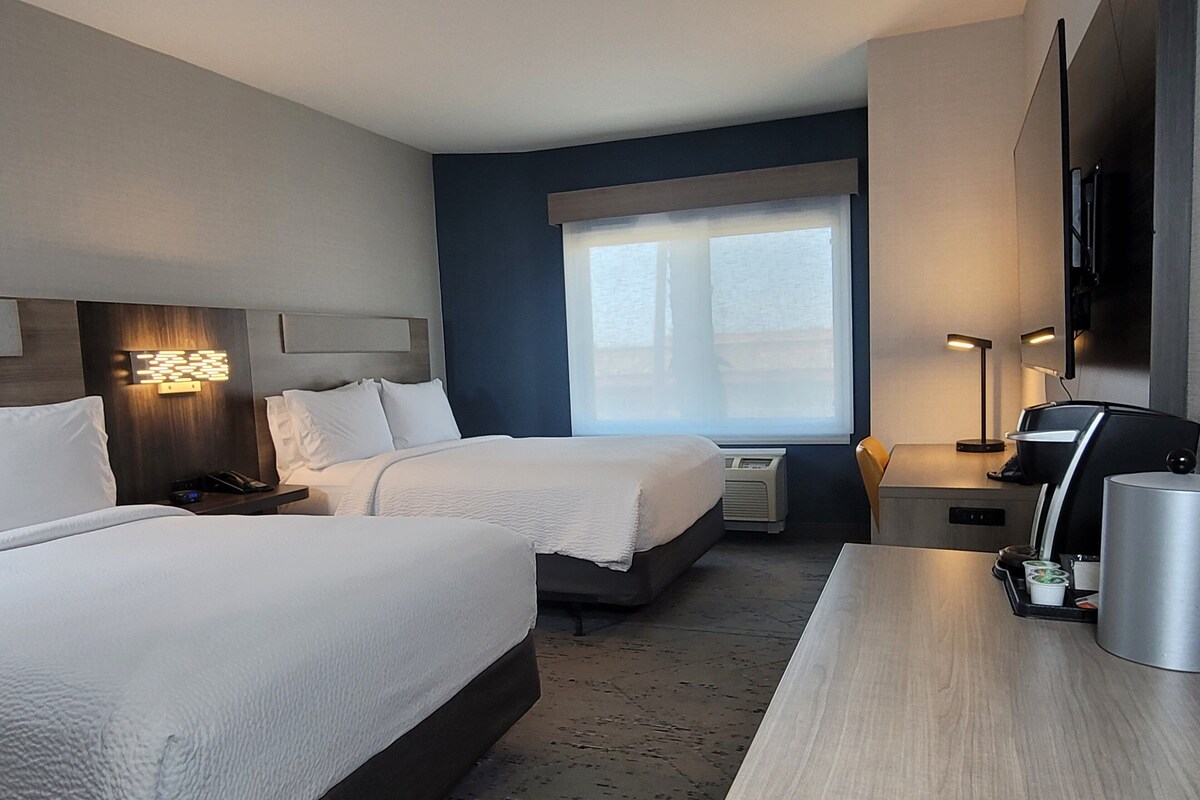 Habitación de hotel con dos camas, un escritorio, una cafetera y un televisor.