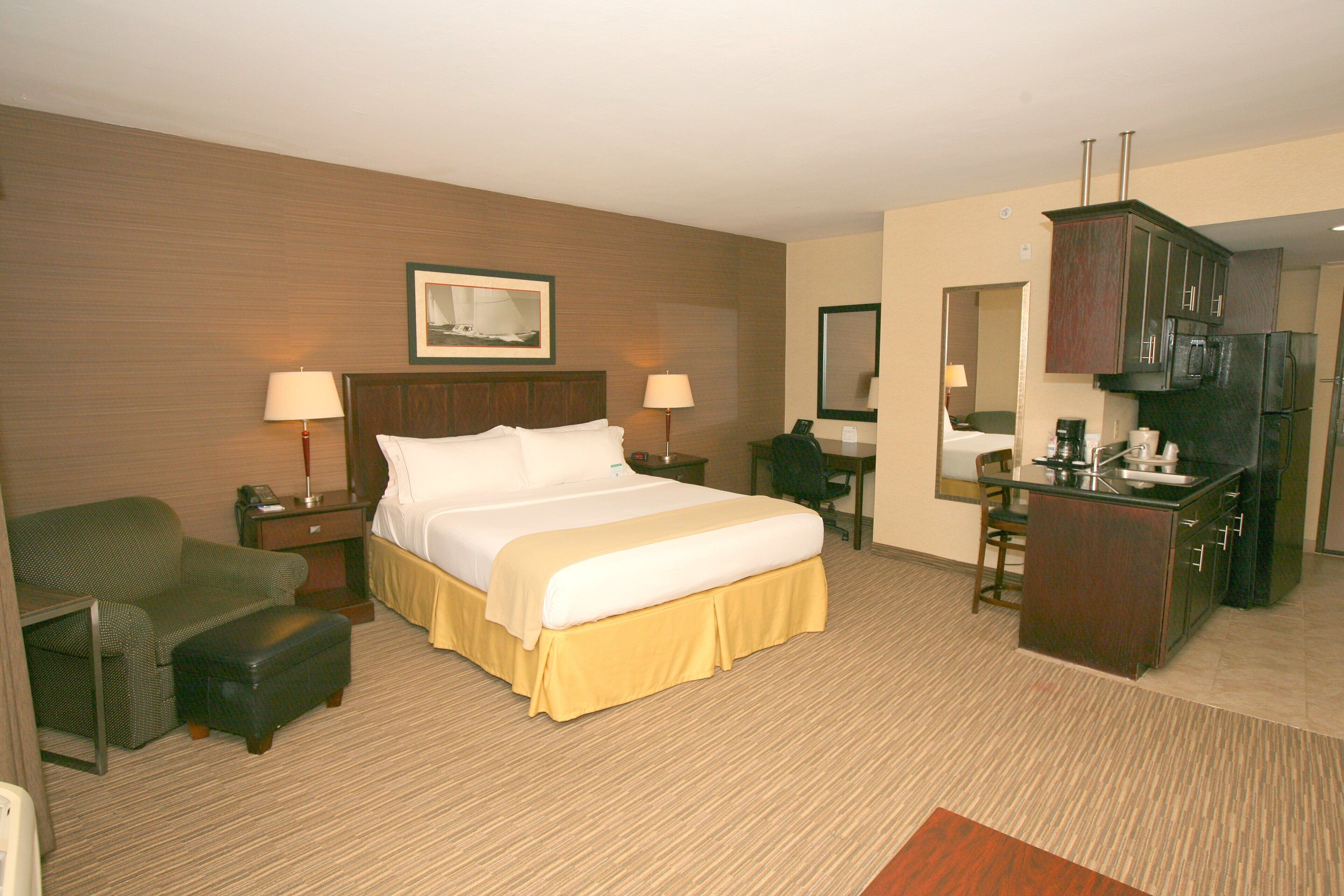 Habitación de hotel con cama, escritorio, silla, pequeño sofá, espejo y kitchenette.