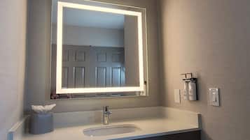 A bathroom with a large mirror, a sink, and a towel dispenser.