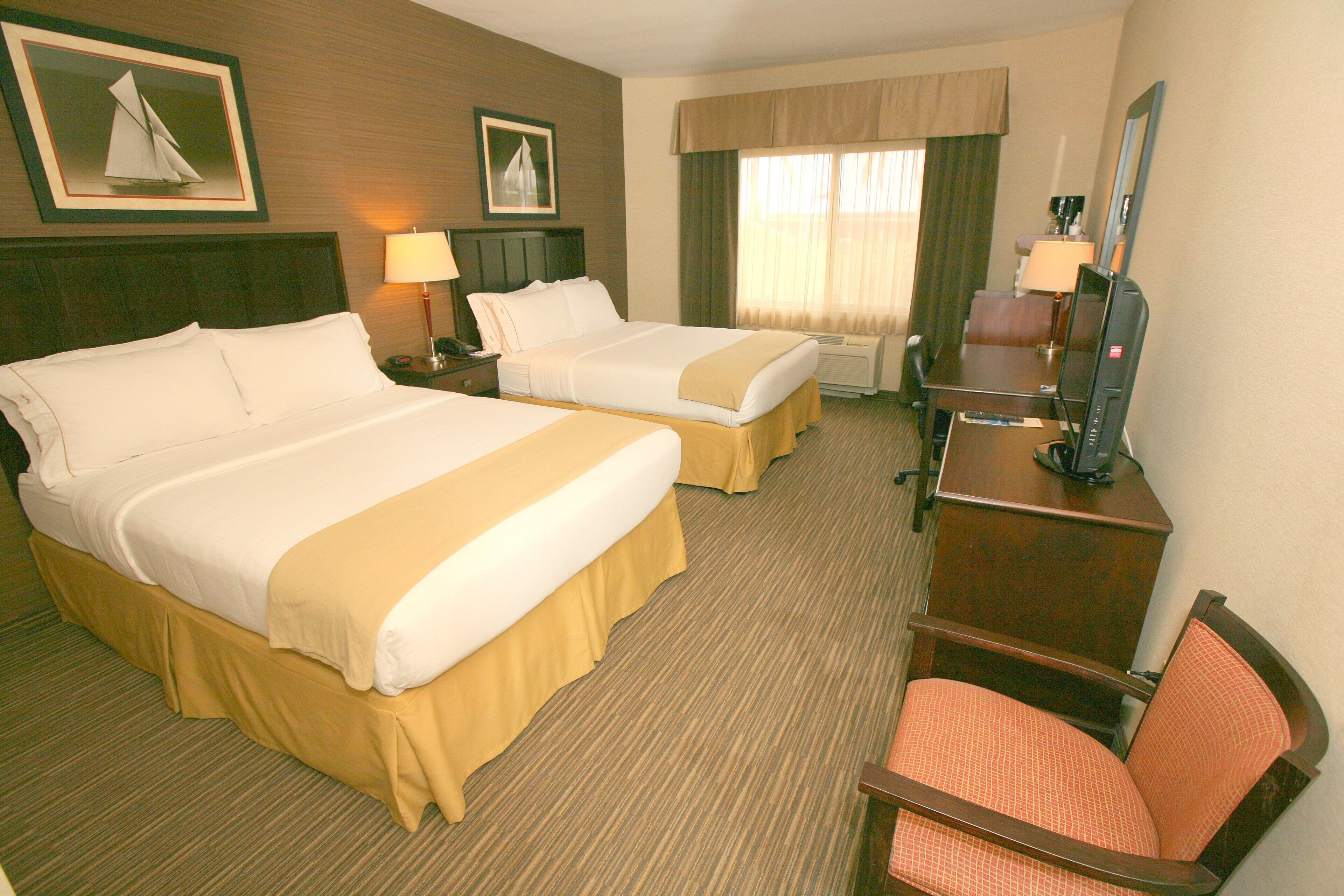 A hotel room with two beds, a desk with a television, and a chair.
