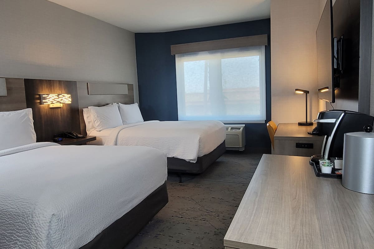 A hotel room with two beds, a desk, a coffee machine, and a TV.