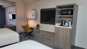 Une chambre d’hôtel avec deux lits, un bureau avec une chaise, une lampe, une machine à café et un téléviseur.