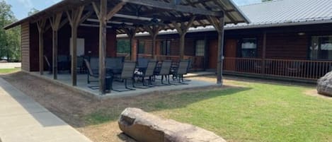 A covered outdoor seating area with tables and chairs, a large rock, and a building with a metal roof.